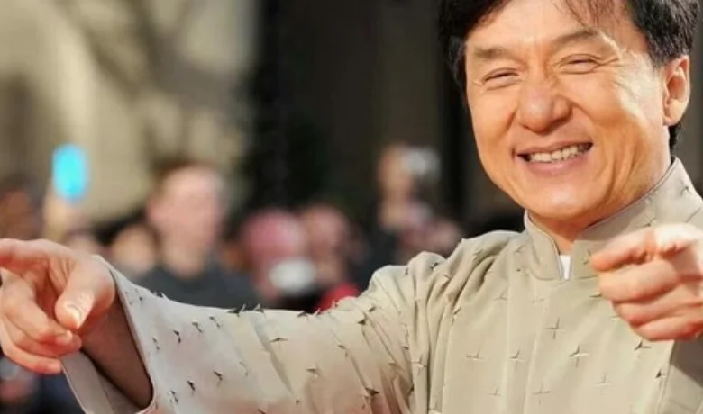 Jackie Chan, aktor dan seniman bela diri Hong Kong yang ikonik, dengan senyum lebar dan menular yang memancarkan keramahan dan energi.