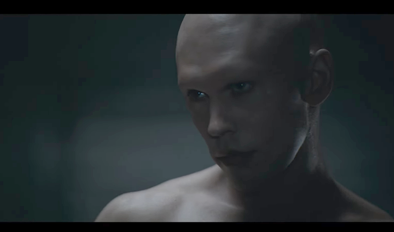 El actor Austin Butler, representado como un joven de piel muy pálida y sin pelo en la cara ni en las cejas, aparece en primer plano, mirando hacia el lado izquierdo de la escena en la tenue luz.